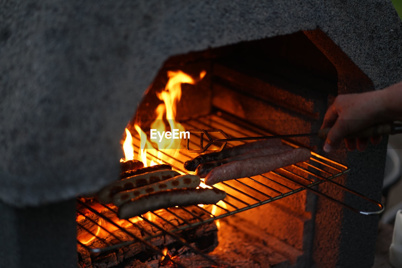 Flipping original thuringian sausages partly in natural casings on an outdoor open flame barbeque g