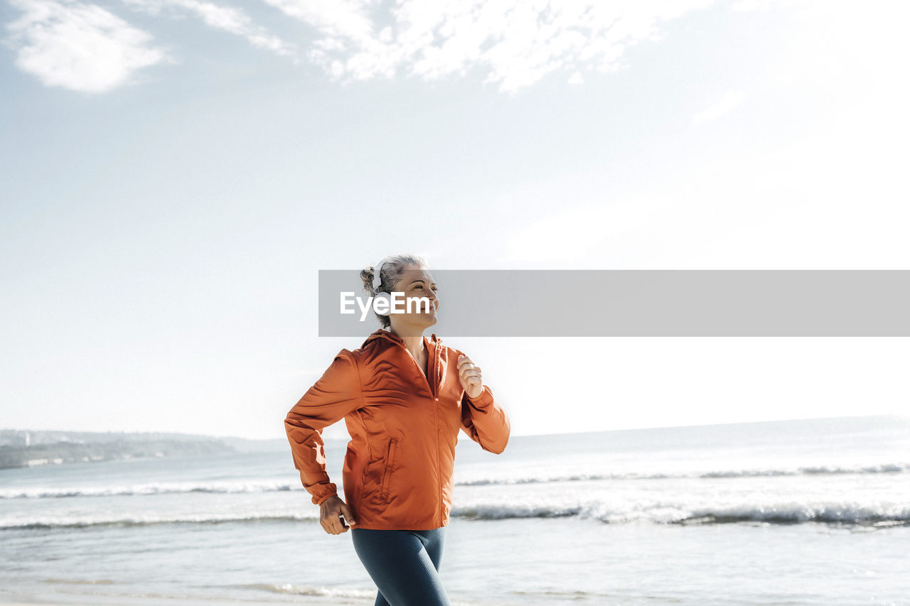 Smiling woman wearing headphones jogging at beach