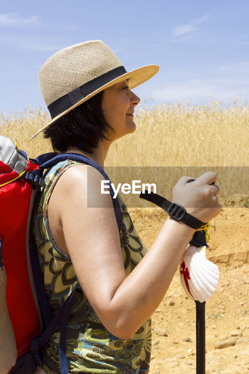 Side view of hiker in hat with backpack standing on hill during sunny day