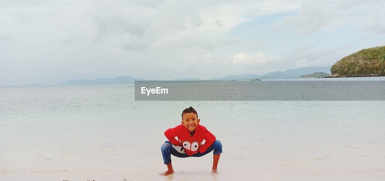 PORTRAIT OF BOY ON BEACH AGAINST SKY