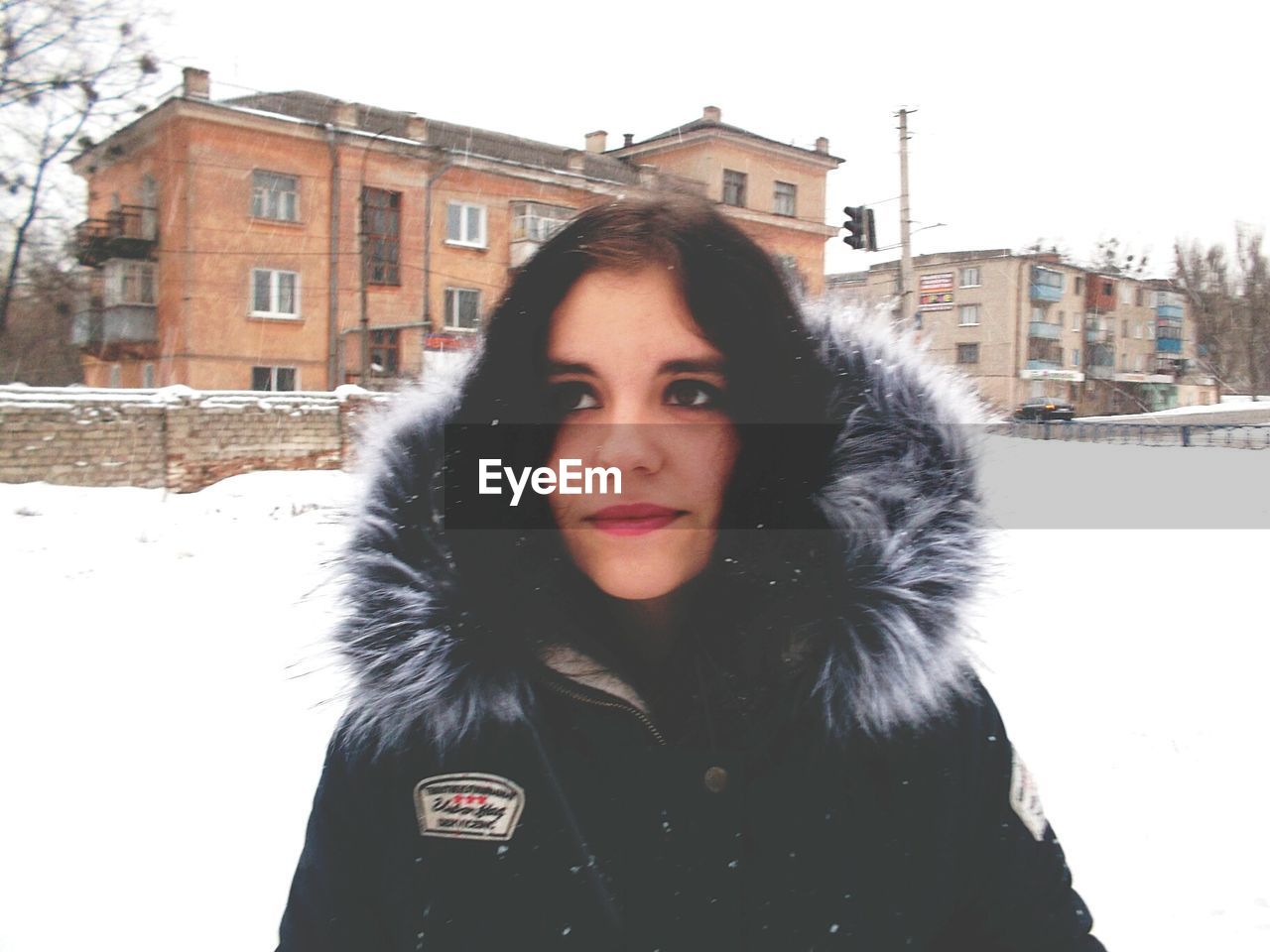 PORTRAIT OF BEAUTIFUL WOMAN STANDING AGAINST SNOW COVERED BUILDINGS