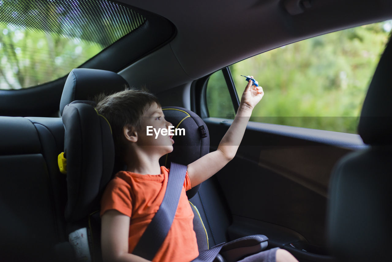 Cute boy playing with toy rocket on back seat of car