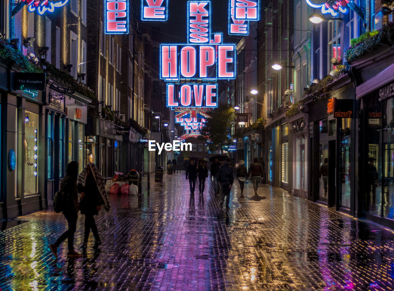 PEOPLE WALKING ON WET ILLUMINATED STREET IN CITY