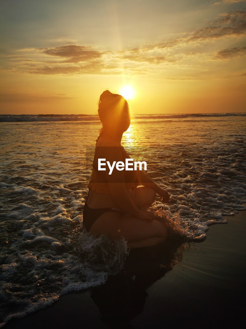 Girl sitting on beach against sky during sunset