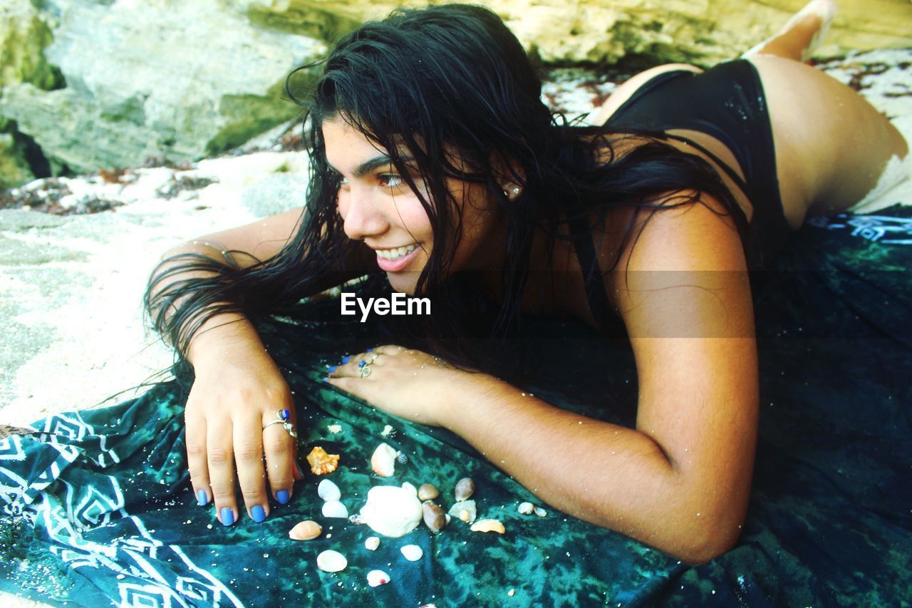 Smiling young woman in bikini lying down at beach