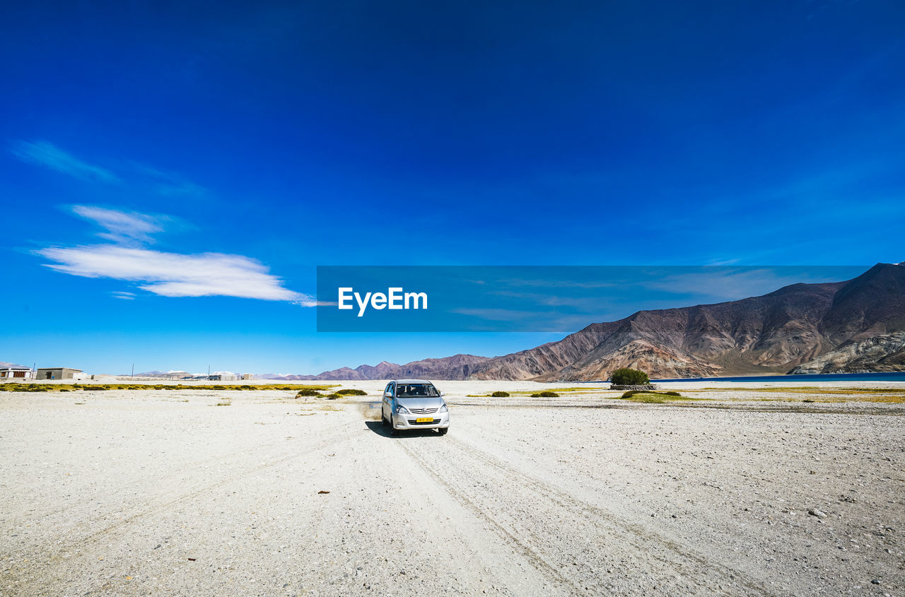 CAR ON ROAD AGAINST MOUNTAINS