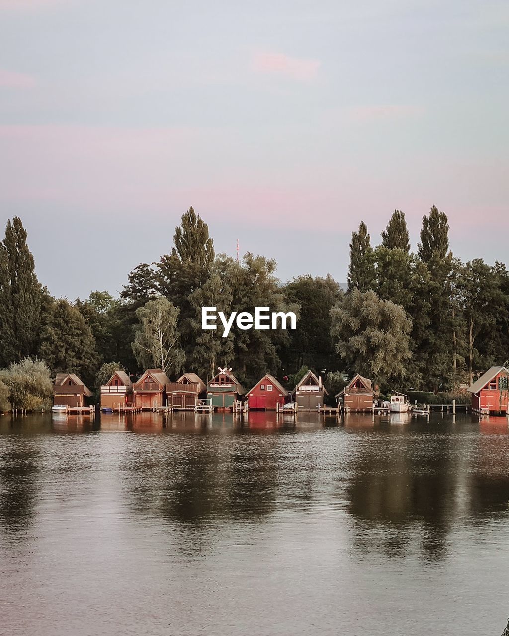 Houses by river against buildings and trees against sky