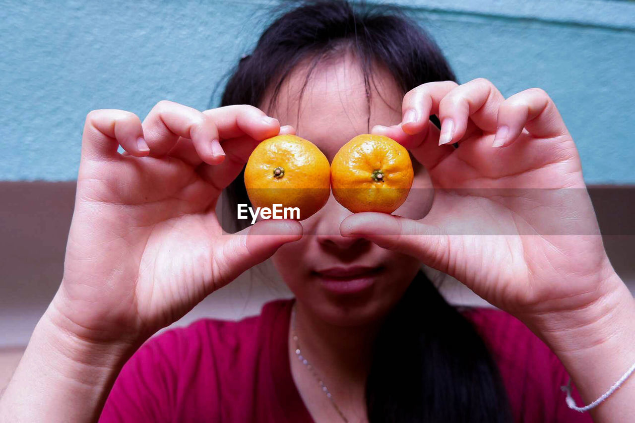 Close-up of woman holding orange over eyes