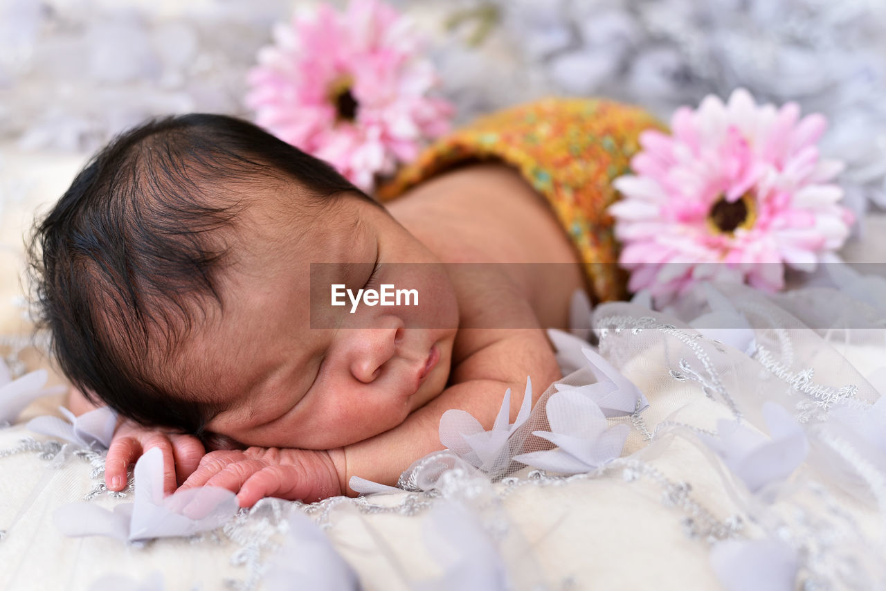 Close-up of cute baby girl with flowers sleeping on bed