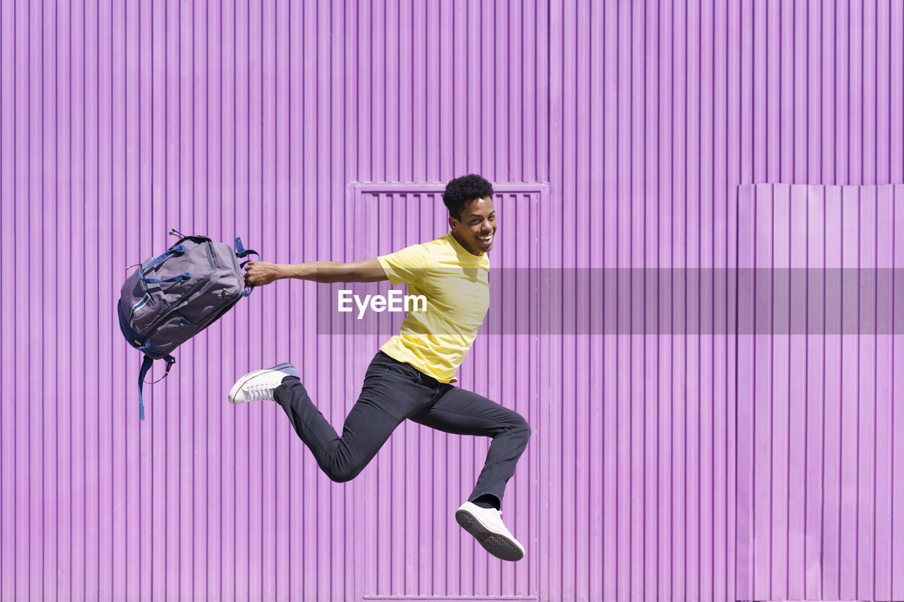 Happy man jumping with backpack by purple cabin