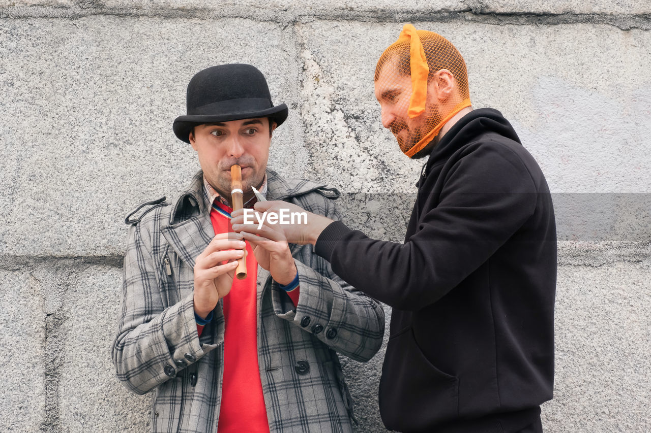 men, adult, clothing, two people, person, holding, city, hat, architecture, wall - building feature, waist up, day, outdoors, standing, young adult, lifestyles