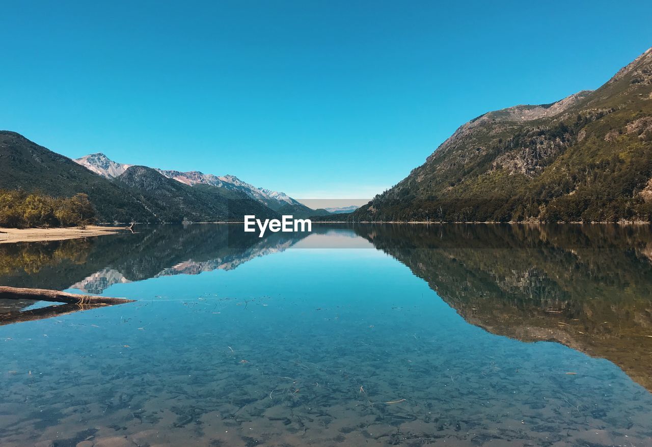 Scenic view of lake and mountains against clear blue sky