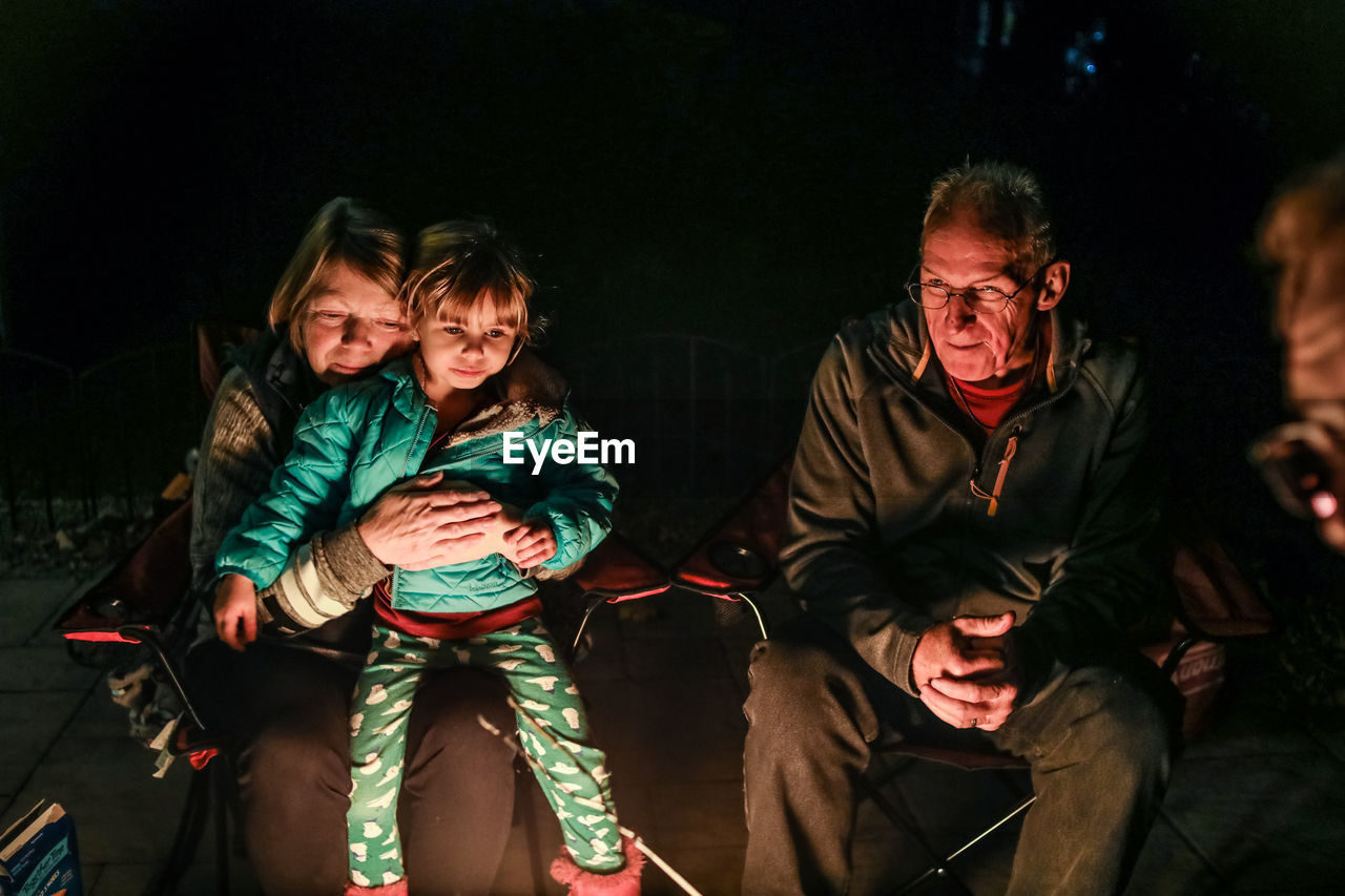 Grandmother hugging grandchild sitting around firepit outside