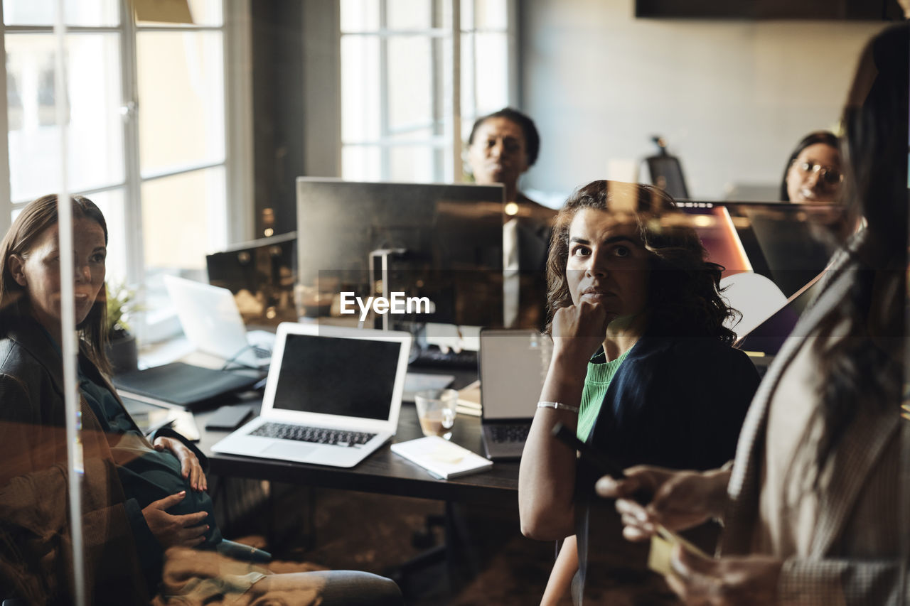 Female colleagues looking at mature entrepreneurs during business meeting in office