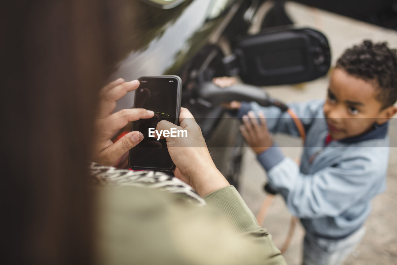 High angle view of boy charging electric car while looking at mother using smart phone