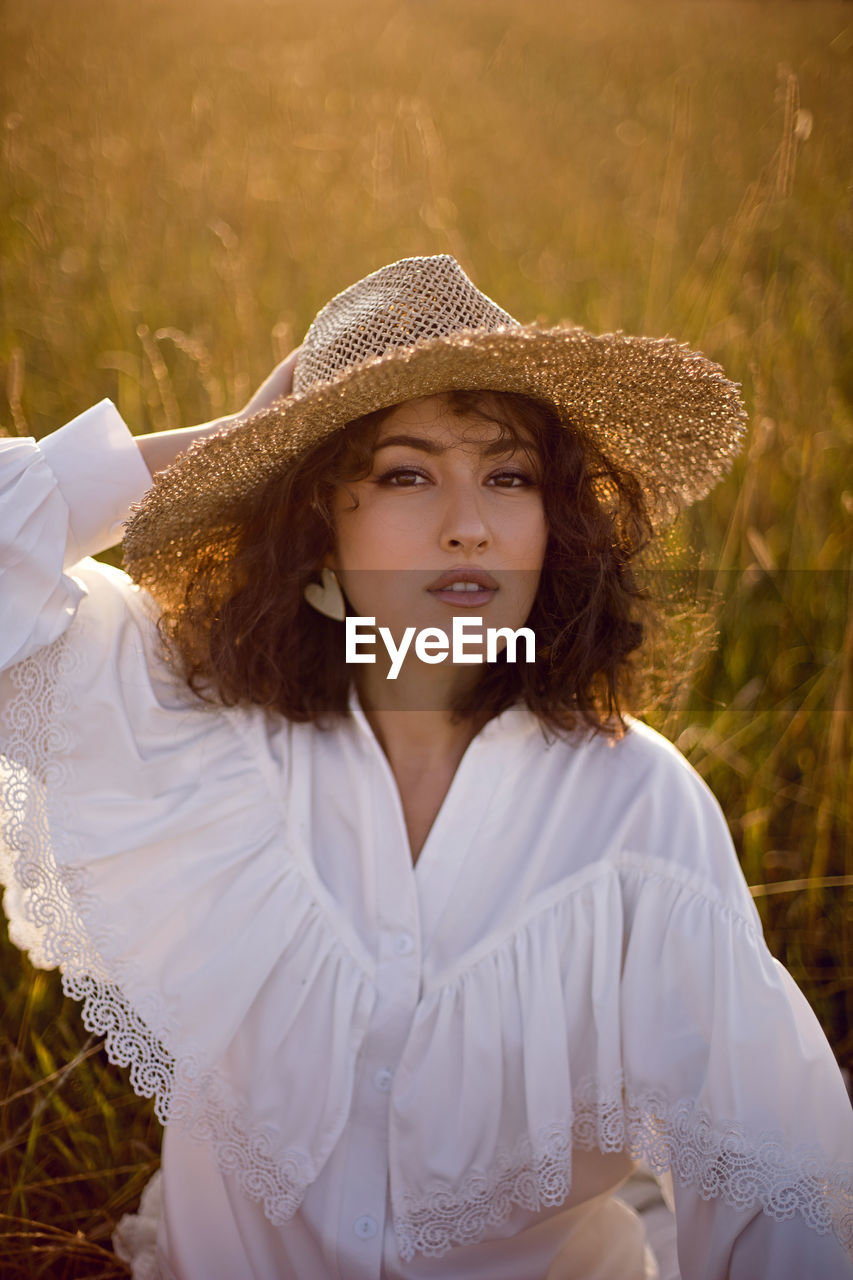  portrait of a curly-haired woman in white clothes and in a wicker hat, grass in autumn