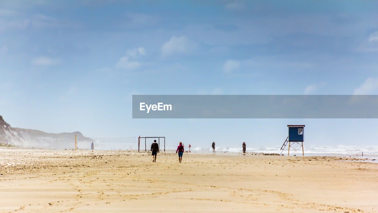 GROUP OF PEOPLE ON BEACH AGAINST SKY