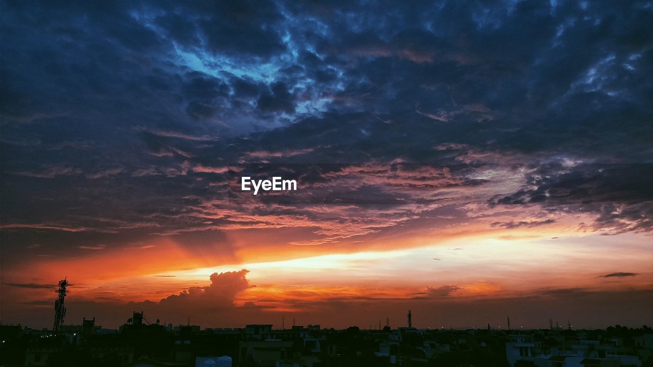 Silhouette trees and cityscape against sky during sunset