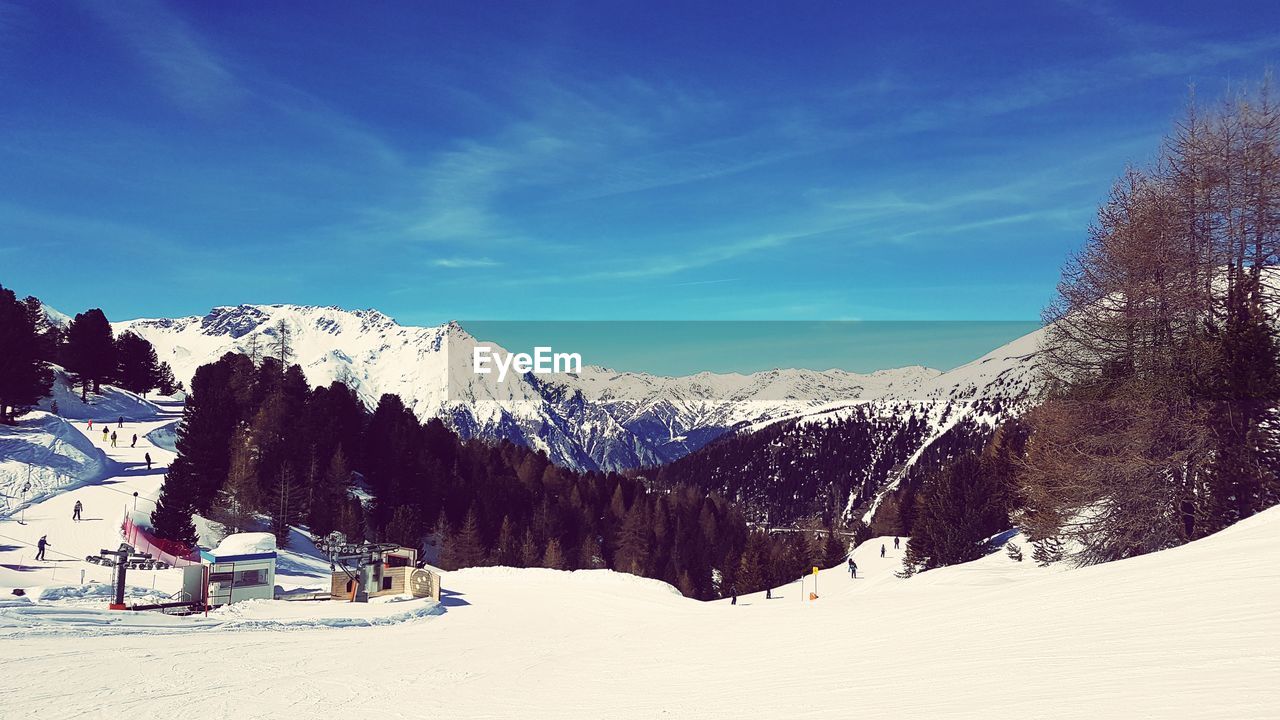 People skiing on snow covered land against blue sky