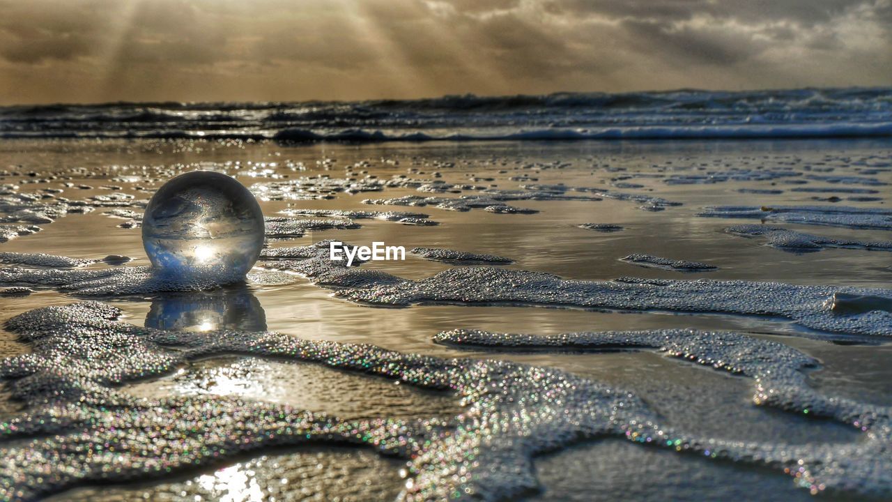 Crystal ball on sea against sky during sunset