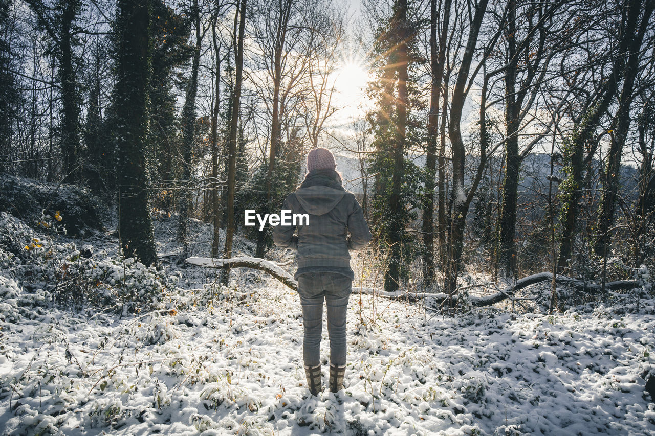 Rear view of woman standing on snow against trees in forest