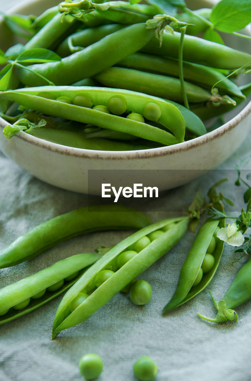 Bowl with young fresh juicy pods of green peas on a textile background. healthy organic food.