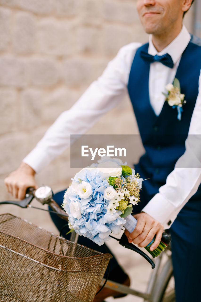 Midsection of groom with bouquet on bicycle outdoors