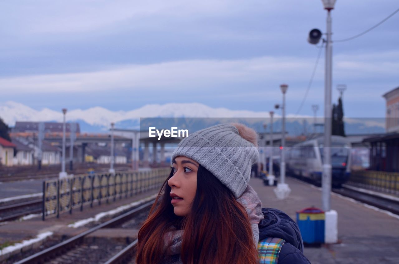 Close-up of woman looking away at railroad station platform against sky