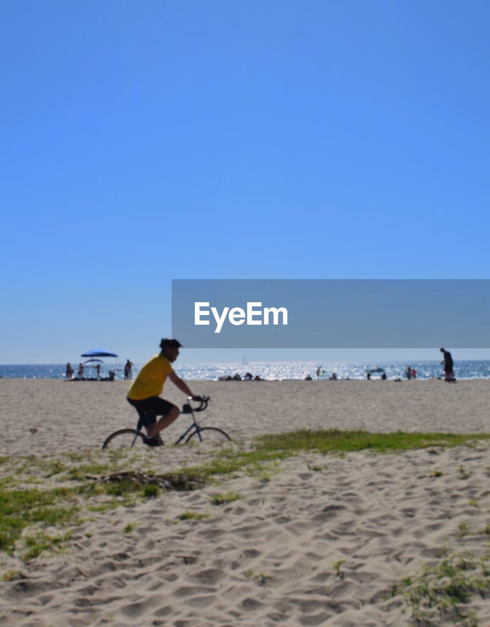 Side view of man riding bicycle at beach against clear sky