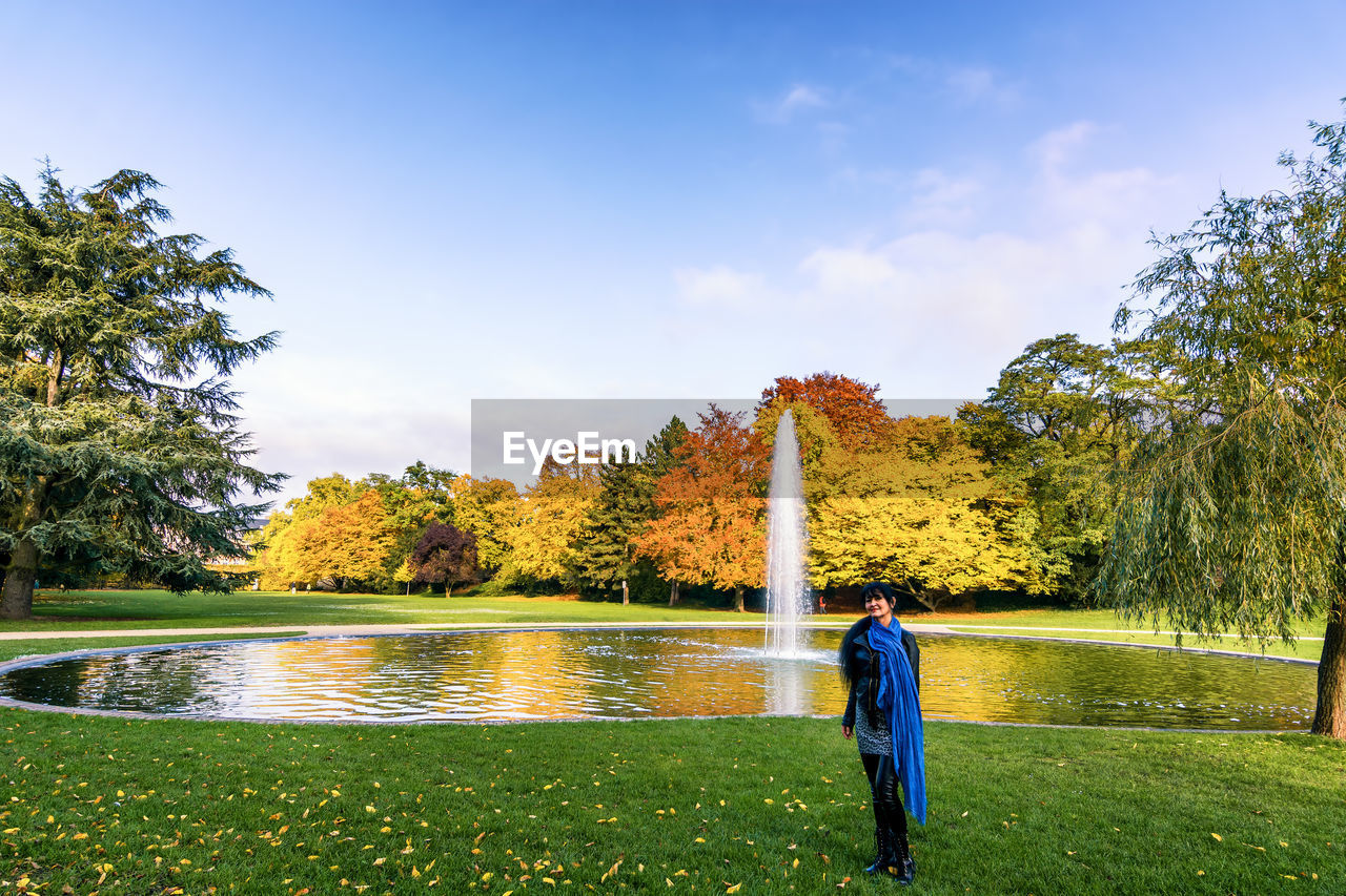 Full length portrait of woman standing by fountain at park