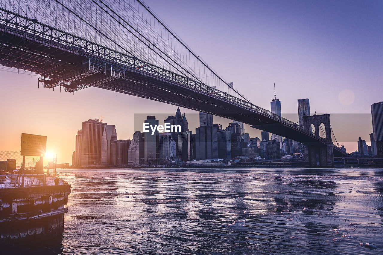 Low angle view of brooklyn bridge by cityscape during sunset