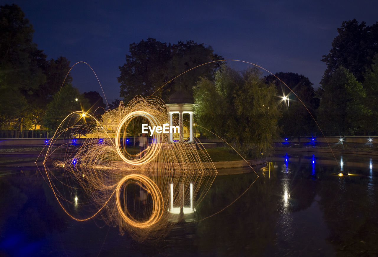 Person spinning wire wool on river at night