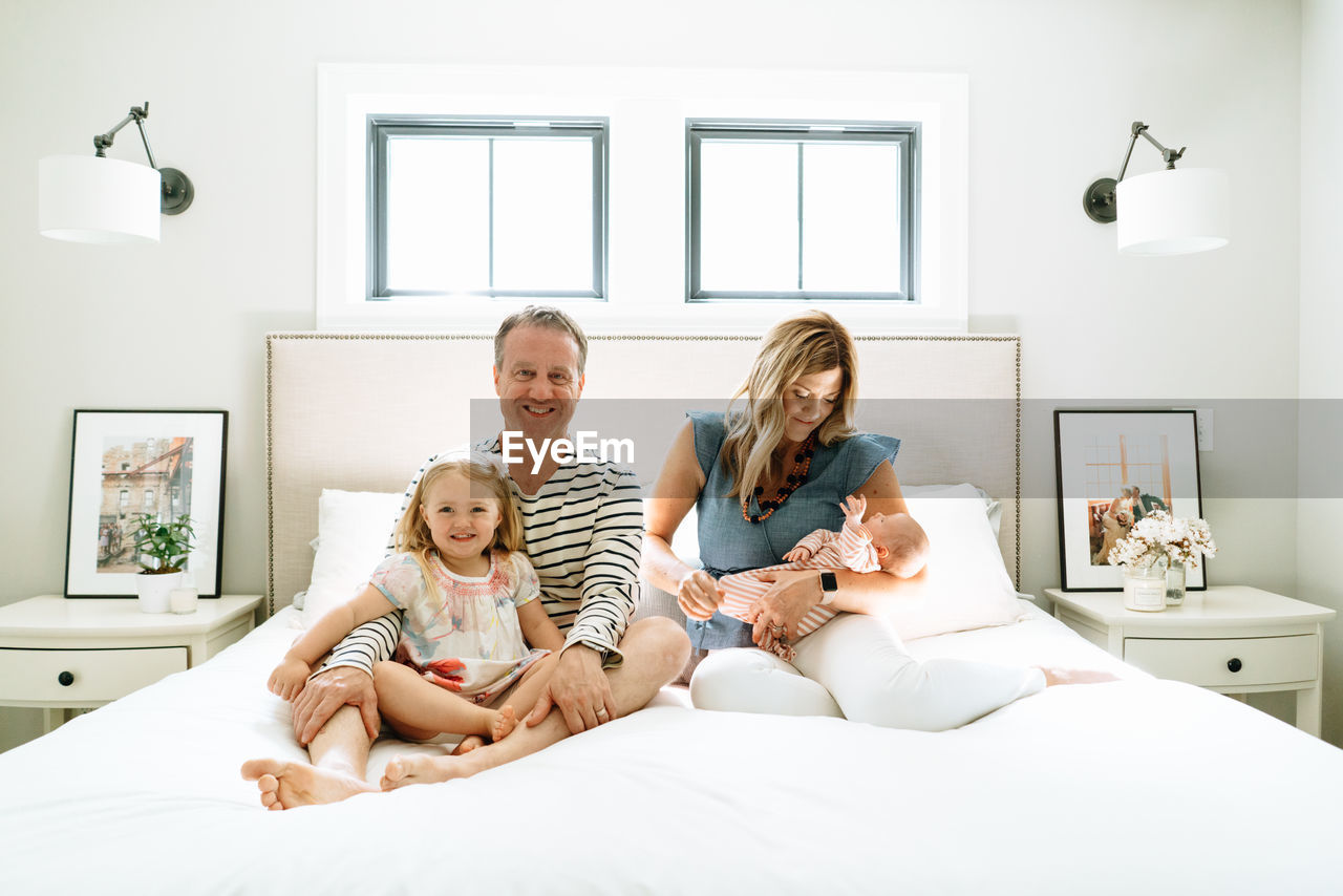 Straight on portrait of a family of four sitting together on a bed