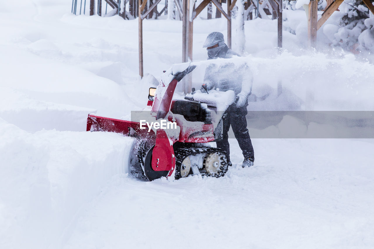 A man using snow blower to clear path in a public park