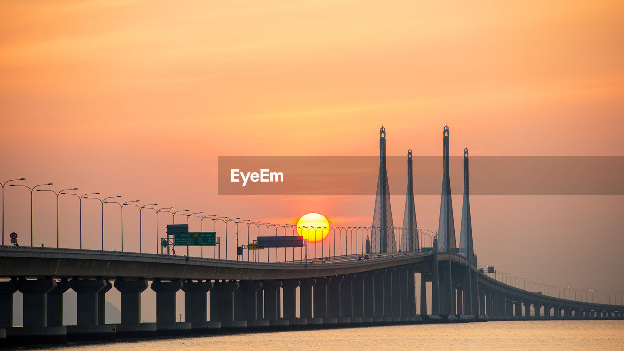 Bridge over water against sky during sunset