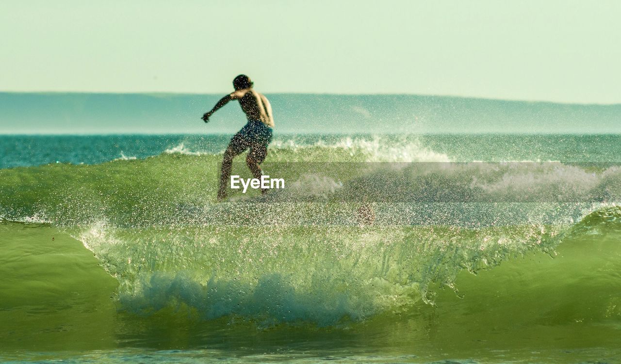 Rear view of man surfing on wave in sea against sky