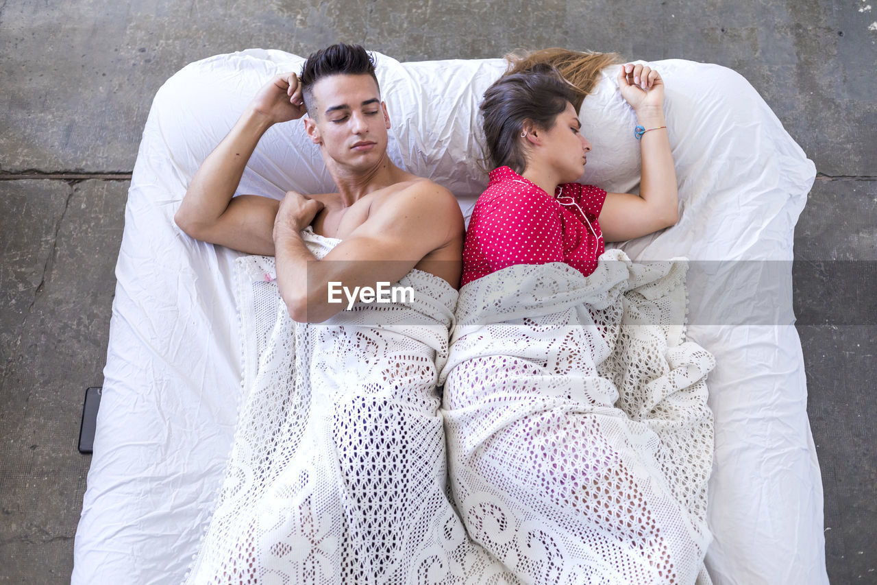High angle view of man and woman sleeping back to back on bed