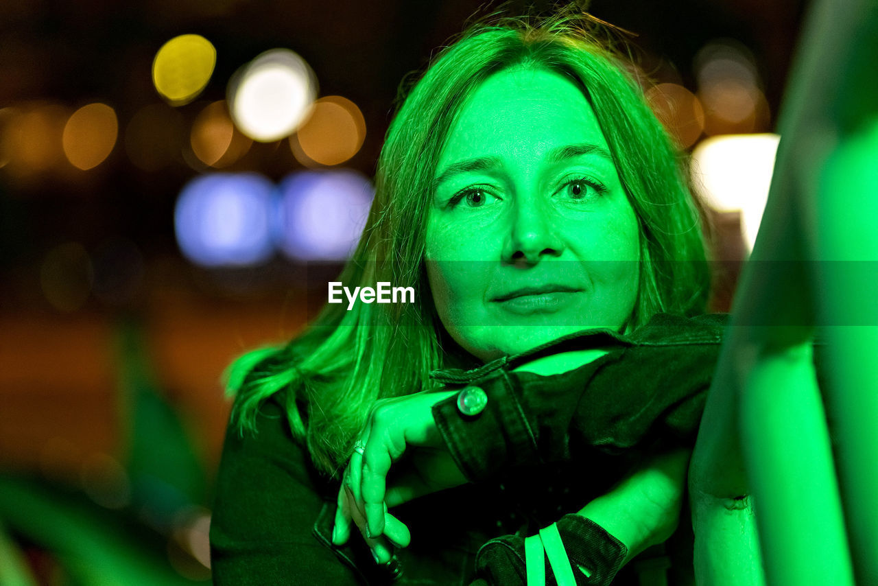 Portrait of a young woman in a night city in neon green on a summer evening. city lights.
