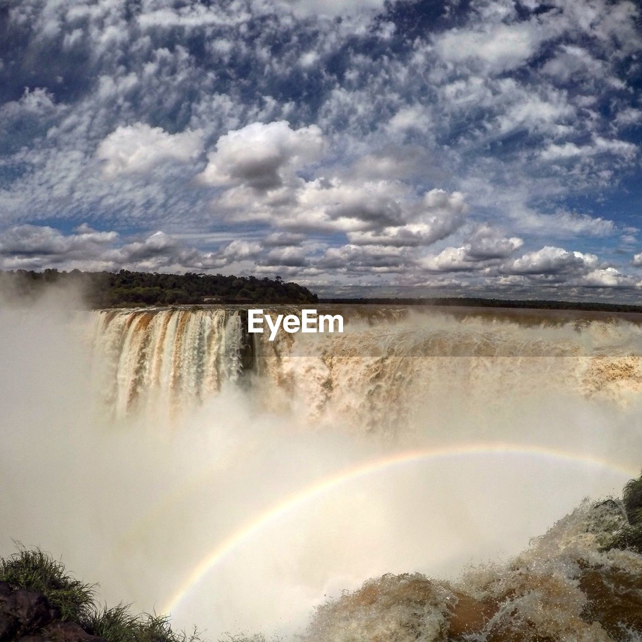 Waterfall and rainbow against cloudy sky