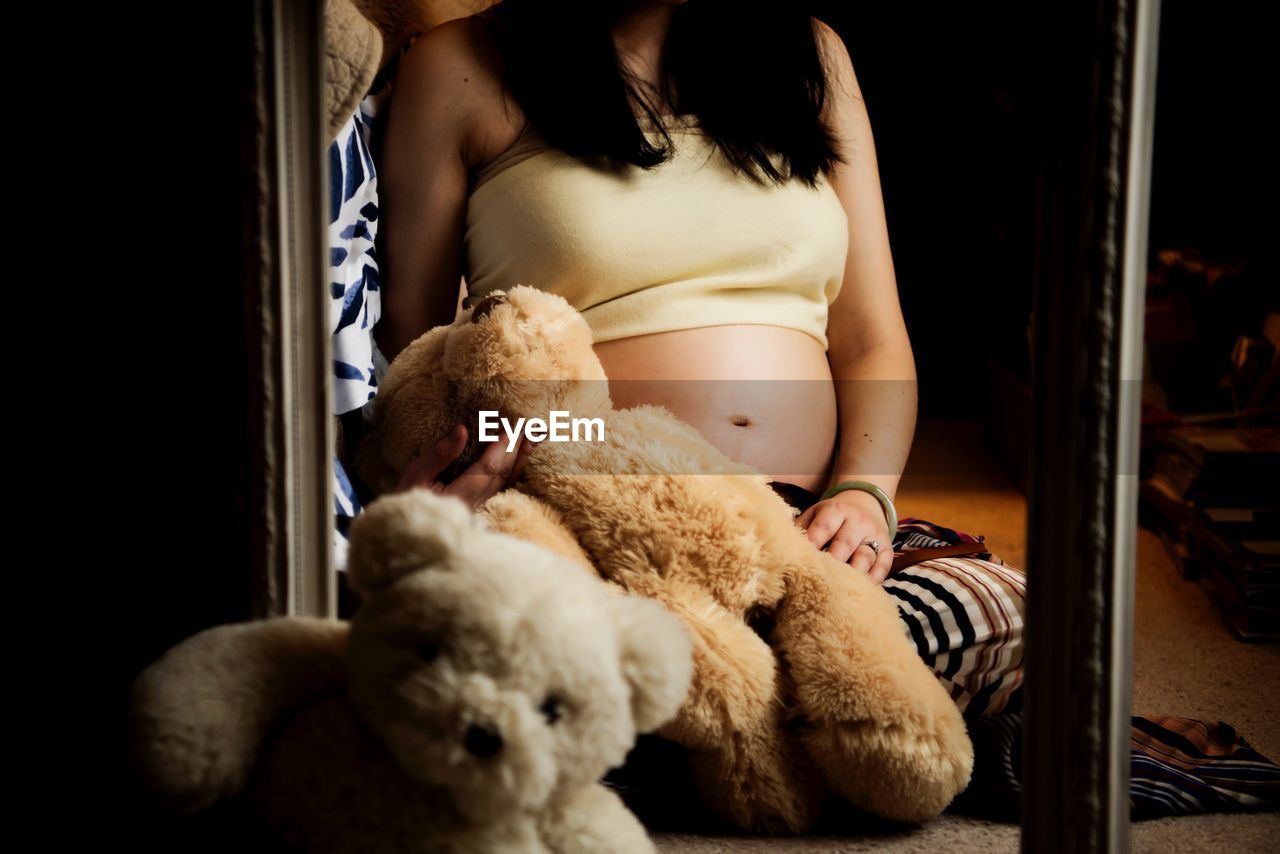 Midsection of pregnant woman with teddy bear sitting at home