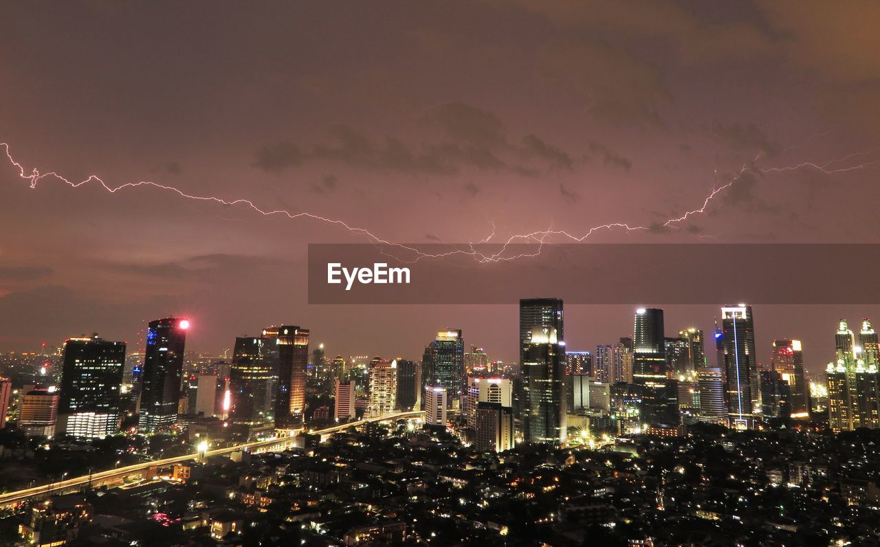 View of lightning over illuminated city at dusk