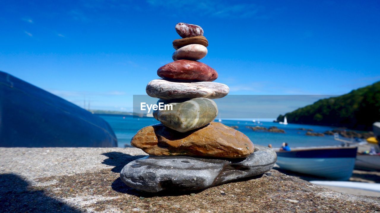 Stack of pebbles in sea against blue sky