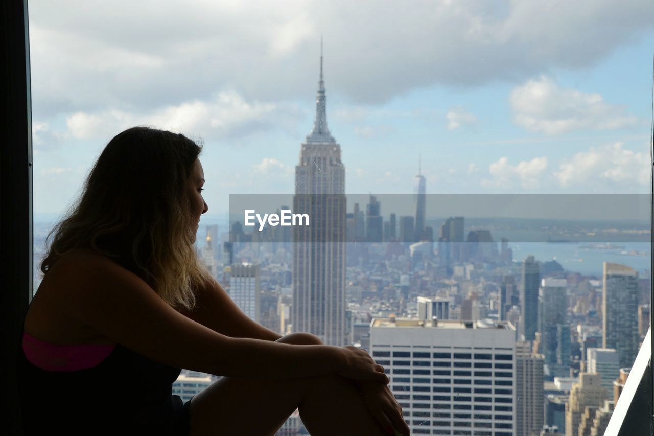 Side view of young woman looking at empire state building in city