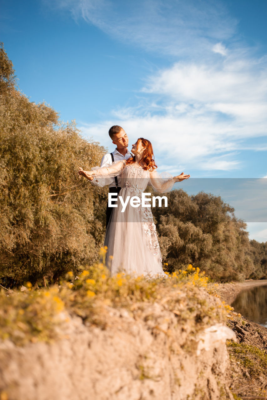 A young wedding couple in love on the edge of a cliff against the backdrop of the river and the sky.