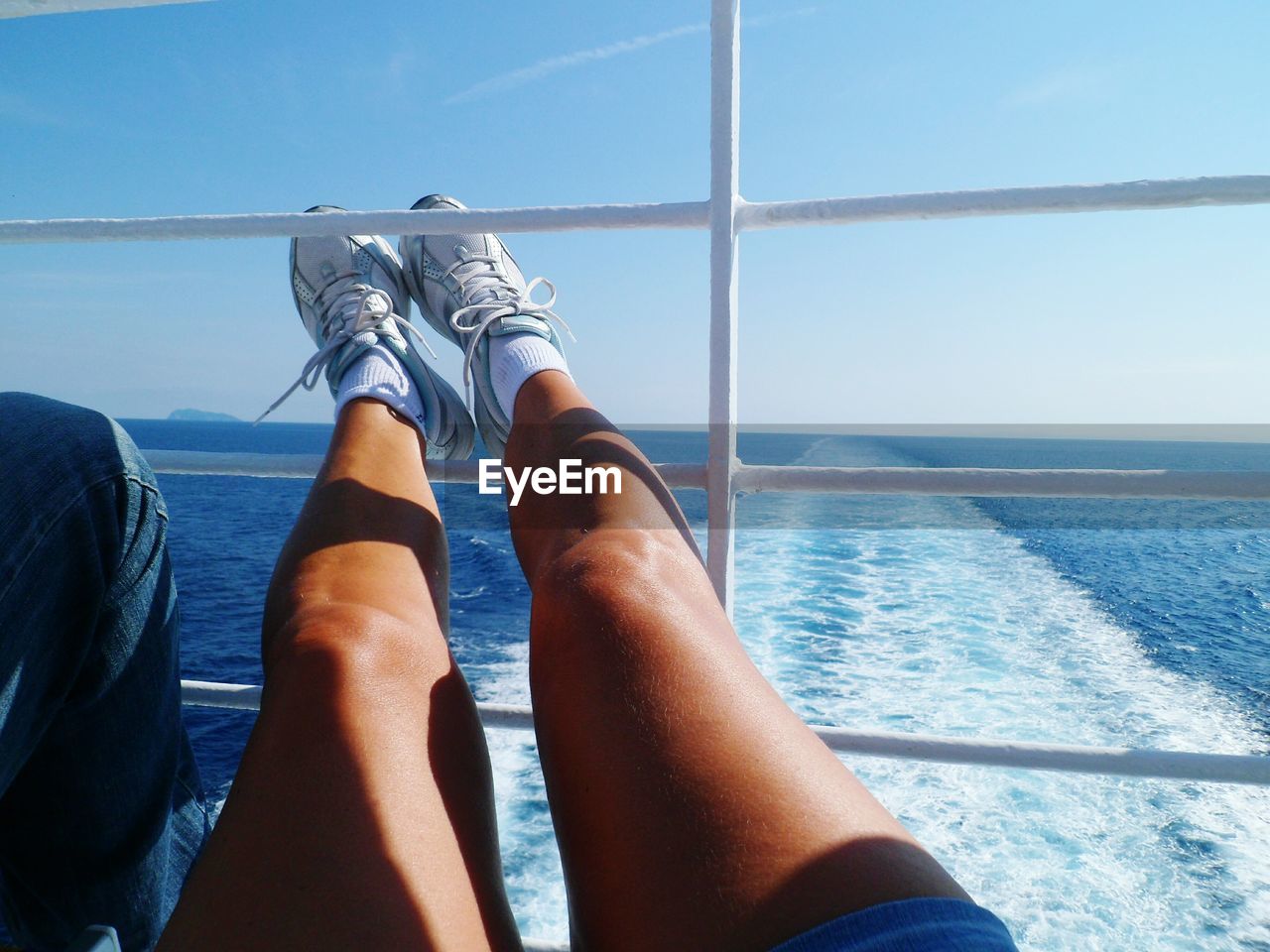 Low section of woman resting legs on railings of boat