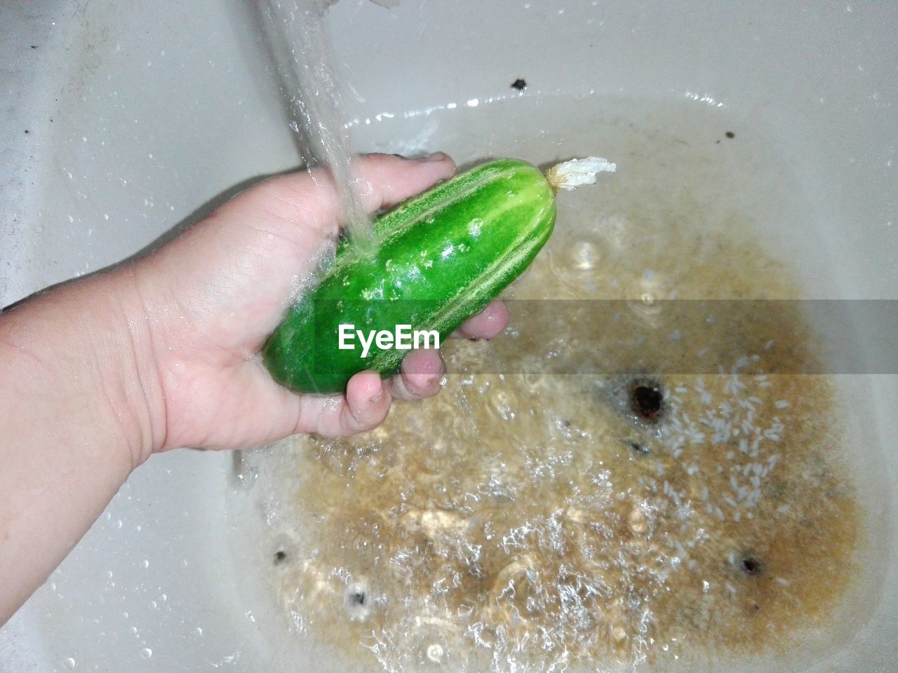 Cropped image of person washing a cucumber