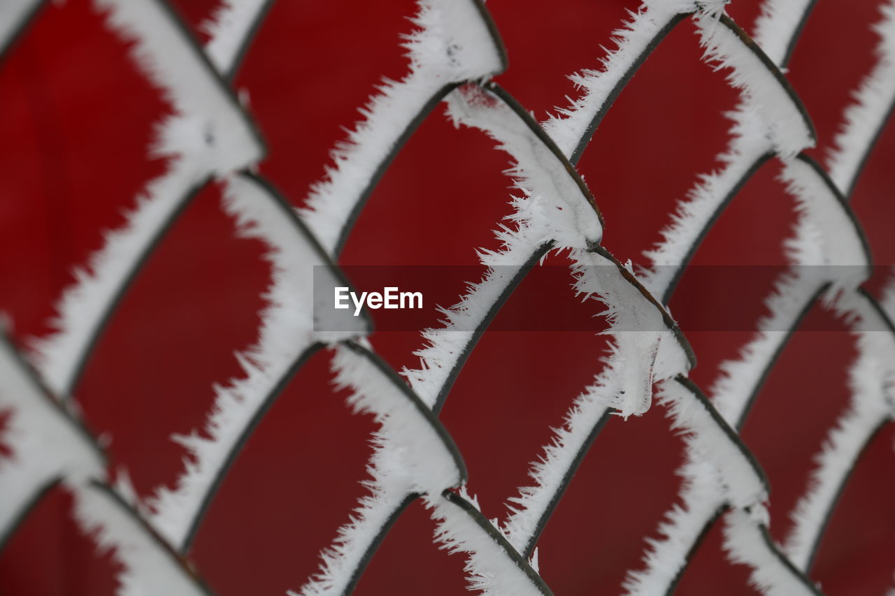 Full frame shot of frost on chainlink fence against red wall