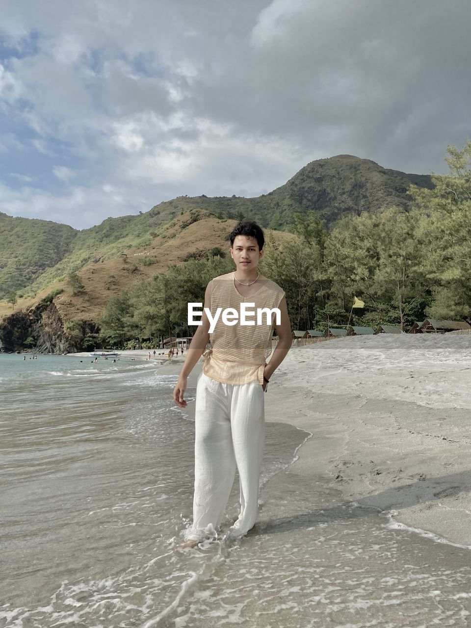 Rear view of young man standing at beach against sky