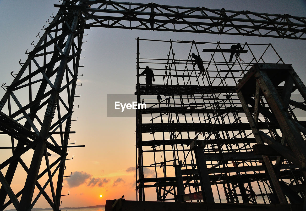Low angle view of workers on silhouette scaffolding against sky during sunset