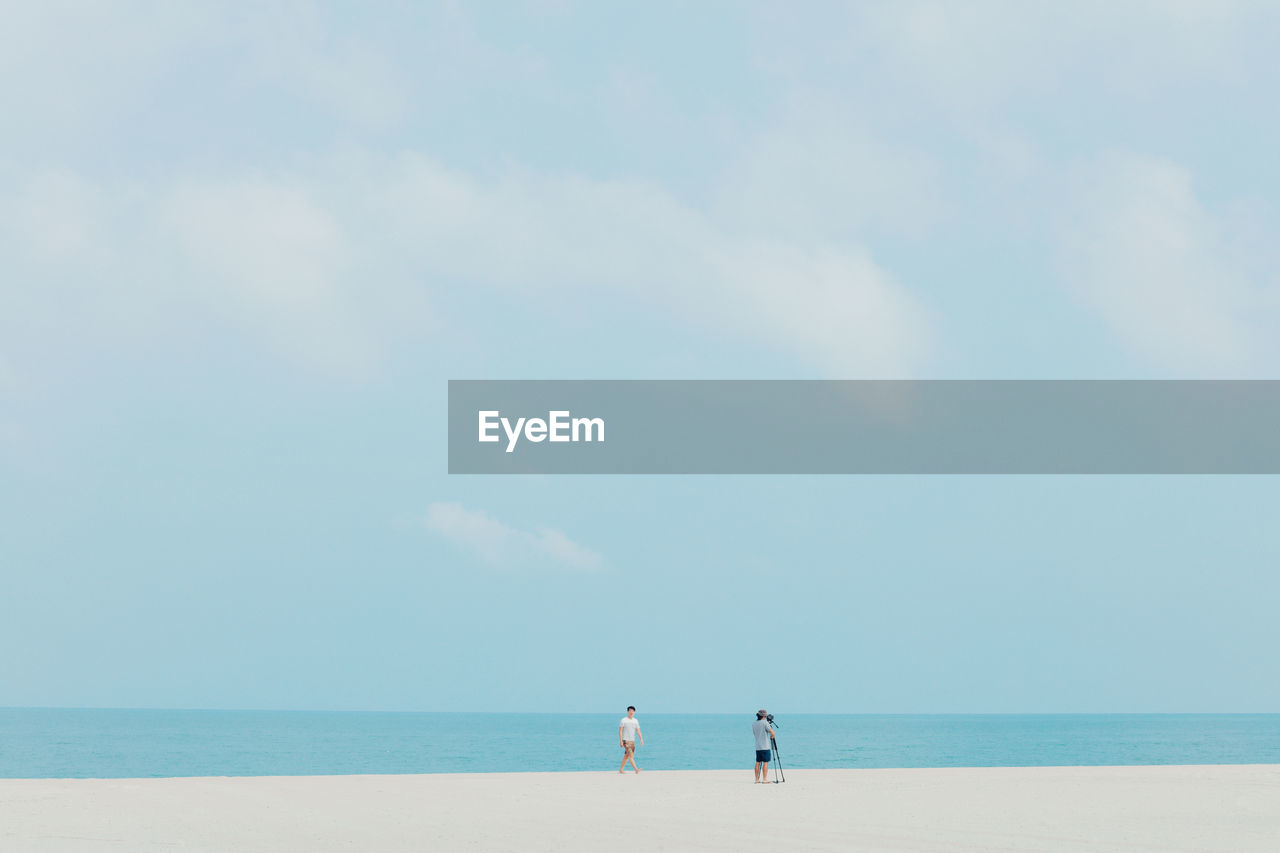 Man with friend photographing at beach against sky